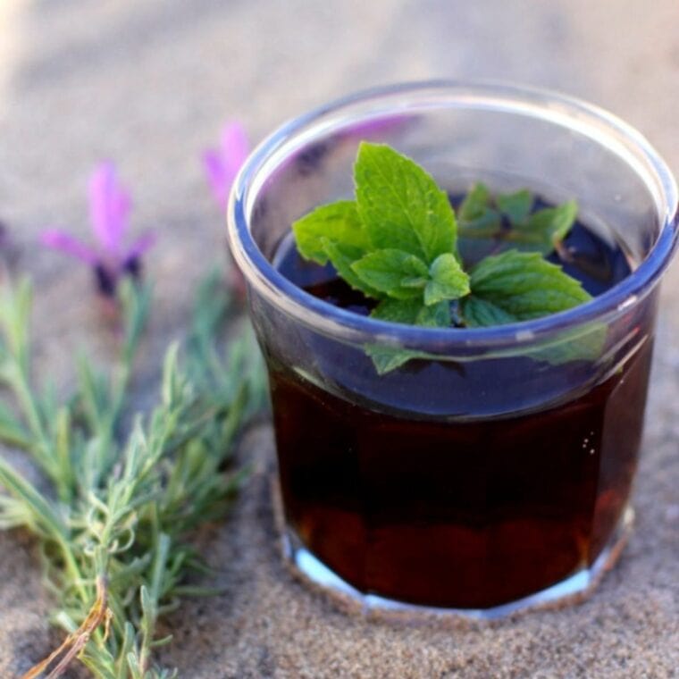 A glass of lavender mint teat with a sprig of fresh mint on top.