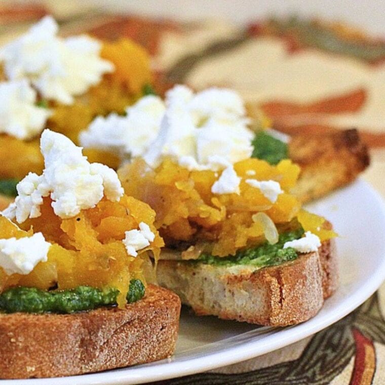Close up photo of pumpkin pesto crostini on a white plate.