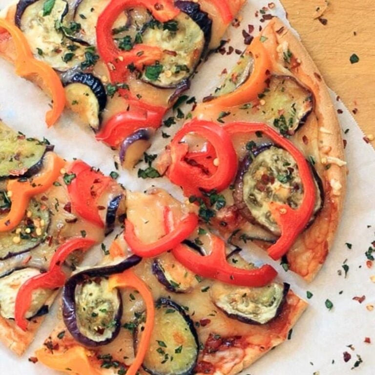 Cheddar cheese pizza topped with eggplant, bell peppers, and herbs on white parchment paper.