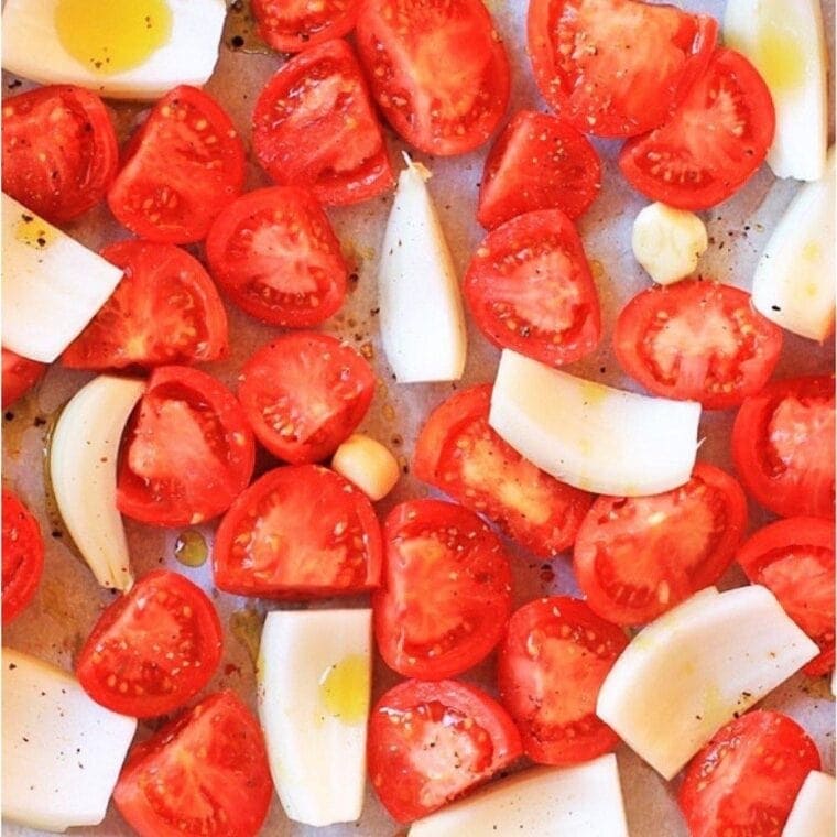 Tomatoes, onions, and garlic on a roasting sheet.