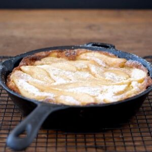 Gluten free pear Dutch baby pancake in a cast iron skillet on w wood tray.