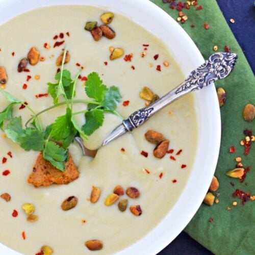 Closeup shot of a bowl of vegan cauliflower soup topped with pistachio nuts and cilantro.