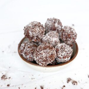 White bowl filled with chocolate energy balls coated in coconut.