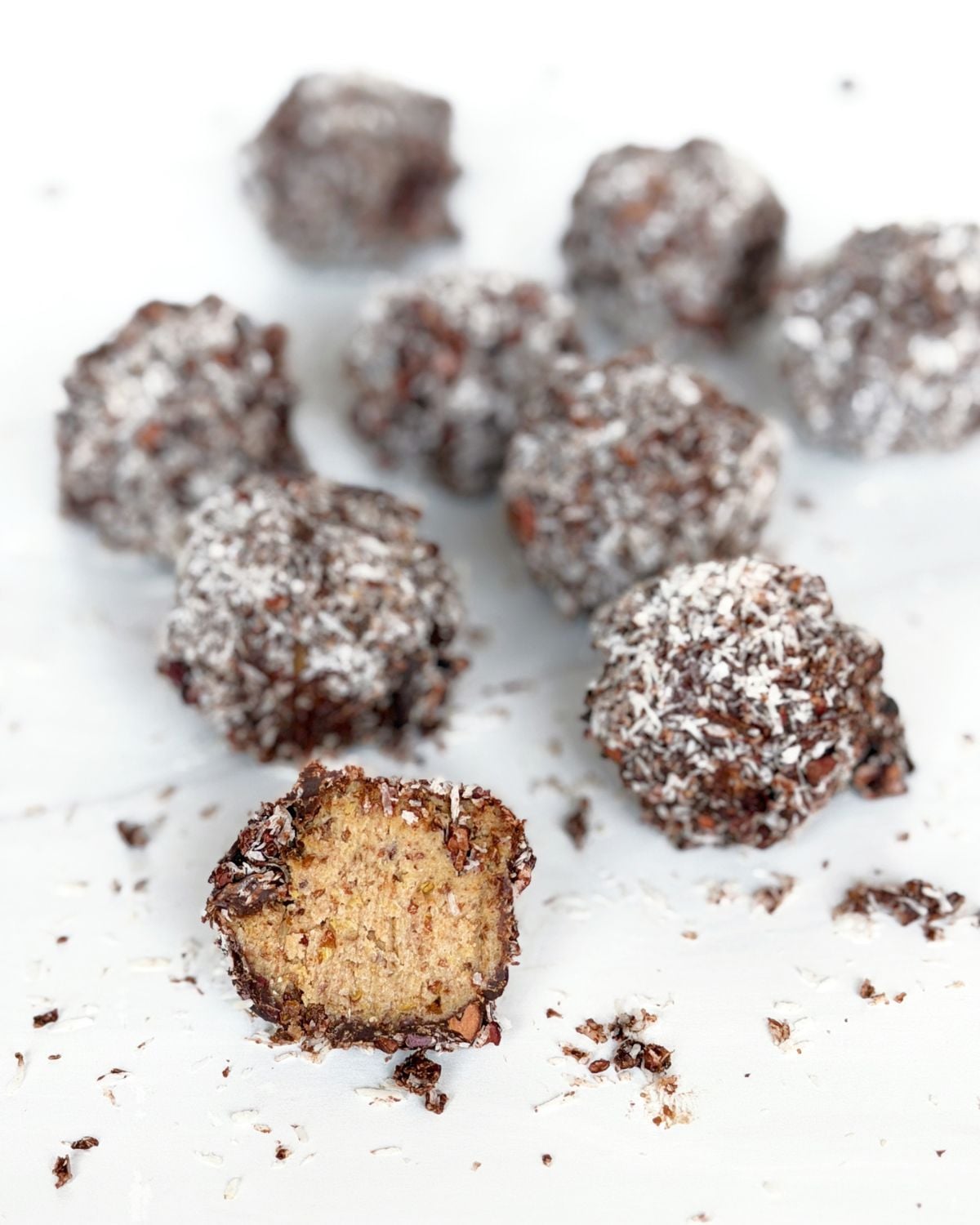 Chocolate energy balls with coconut on a white tray. One ball in the front has a bite out of it.