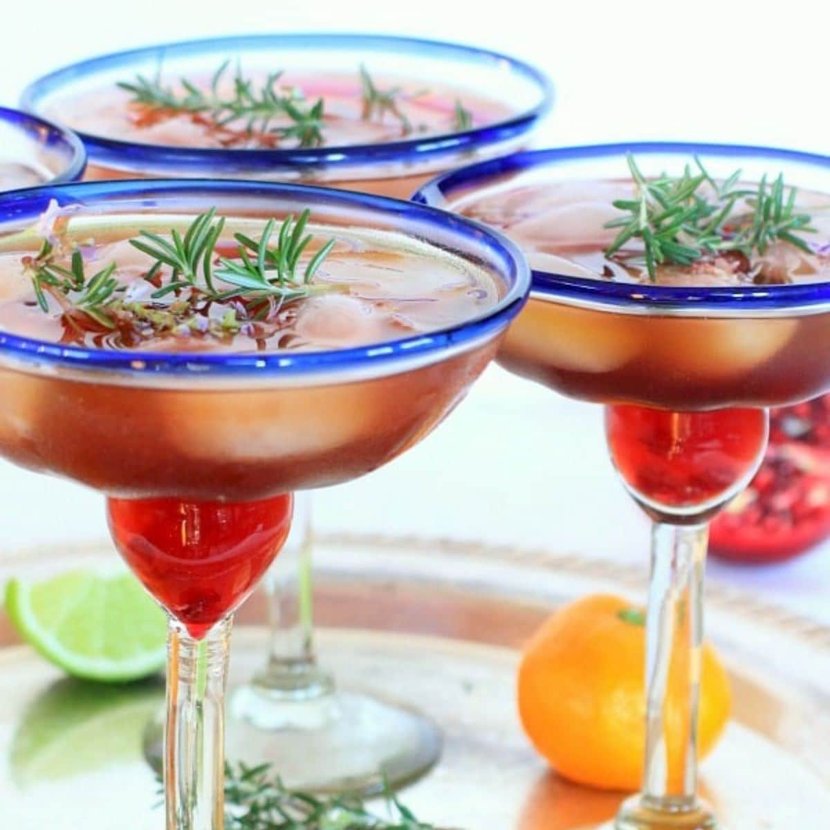 3 blue rimmed margarita glasses filled with rosemary pomegranate margaritas.