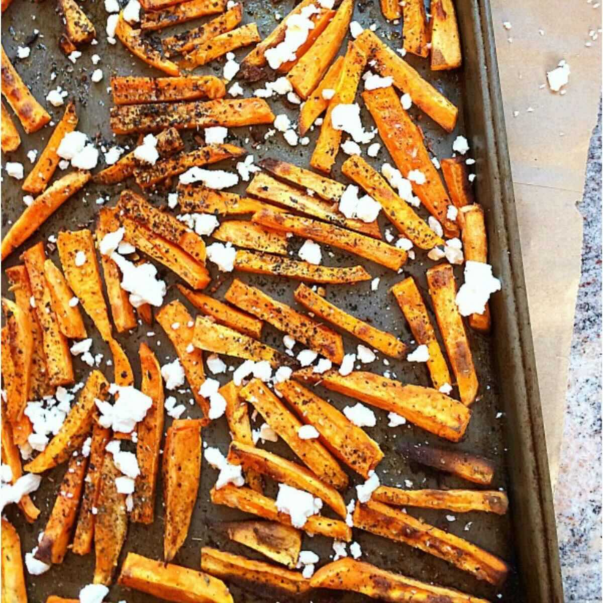 Baking sheet with gluten free sweet potato fries topped with feta cheese and Greek herbs.