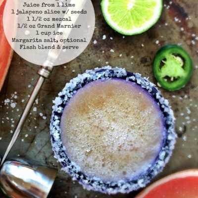 mezcal margarita in a blue rimmed glass on a tray with lime, salt, and jalapenos