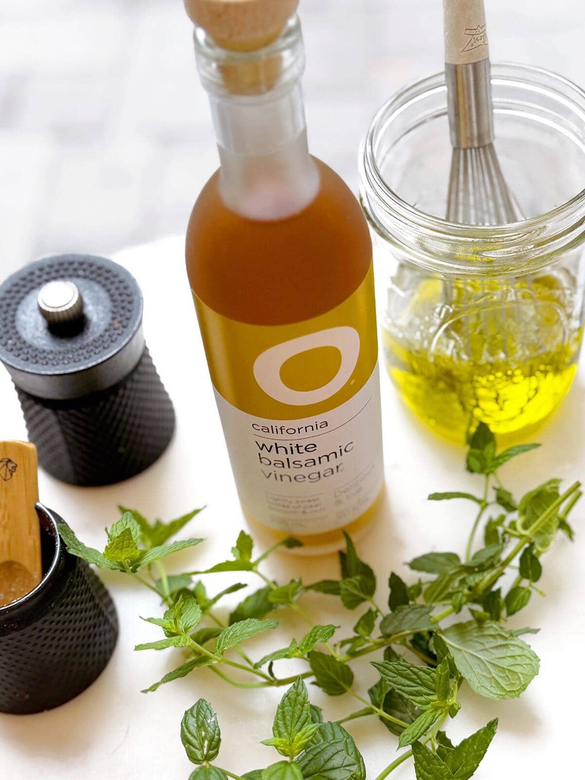 White tray with olive oil, white balsamic vinegar, salt, pepper, and fresh herbs.