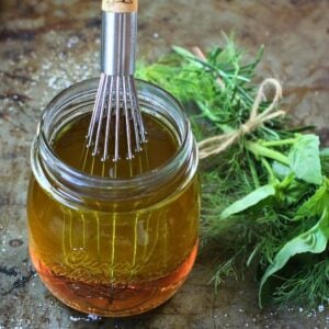 Mason jar with white balsamic vinaigrette and a whisk. Fresh herbs in the background.