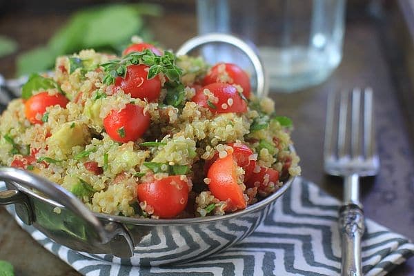 Quinoa salad with tomatoes, oregano, and avocado in a silver serving bowl.