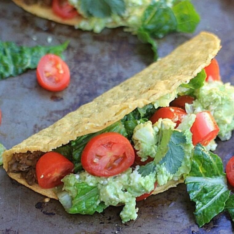 Close up photo of lentil tacos filled with lentil taco meat, guacamole, lettuce, and tomato.