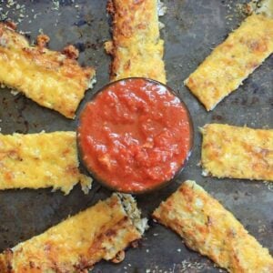 Cauliflower breadsticks on a tray with a bowl of marinara dipping sauce.