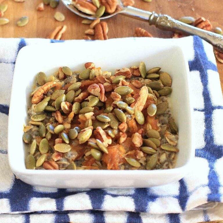 White bowl with chia oatmeal topped with pumpkin seeds and pecans.