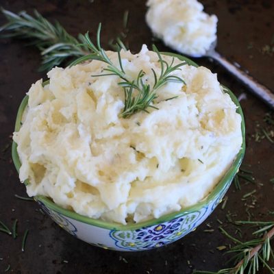 Healthy mashed potatoes with rosemary in a serving bowl.