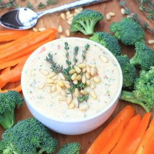 Healthy queso recipe in a white bowl, surrounded by lots of colorful vegetables.