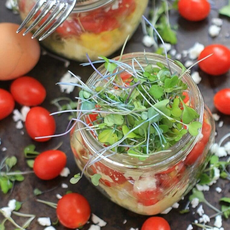Microwave scrambled eggs in a jar topped with feta cheese, tomatoes, and microgreens.