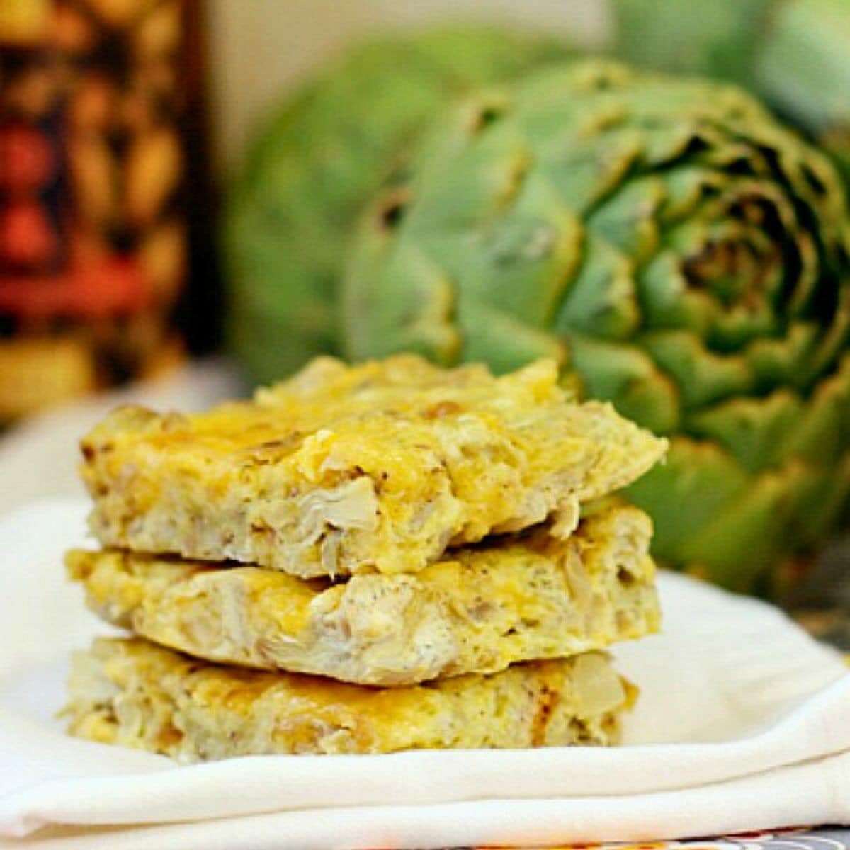 Three artichoke squares stacked up on a white napkin.
