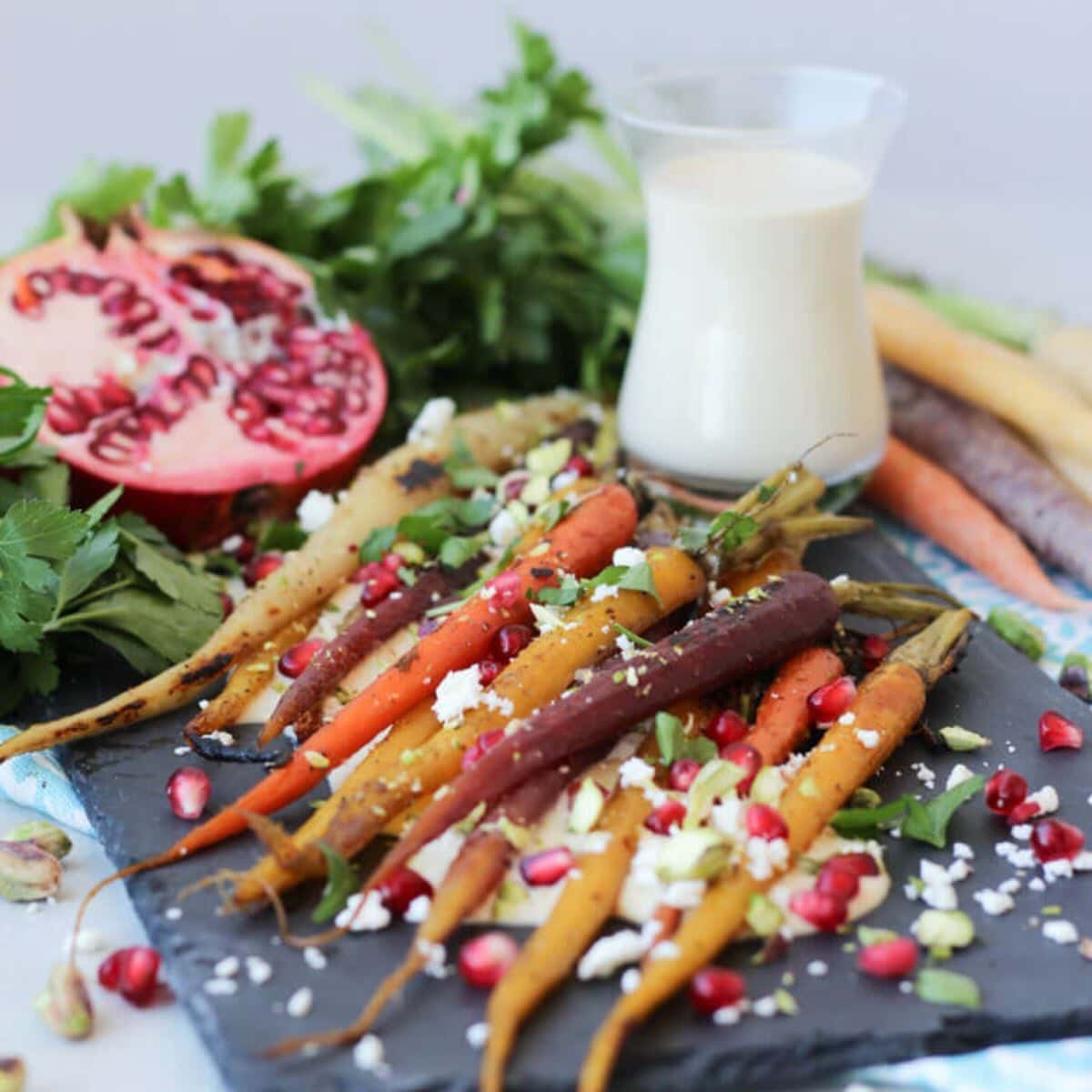 Platter of colorful roasted carrots topped with herbs, pomegranate arils, and cheese.