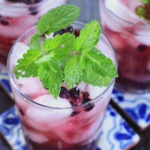 Glass filled with wild blueberry ginger mint green iced tea topped with fresh mint.