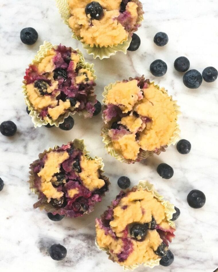 Gluten free blueberry muffins on a white marble tray with fresh blueberries in the background.