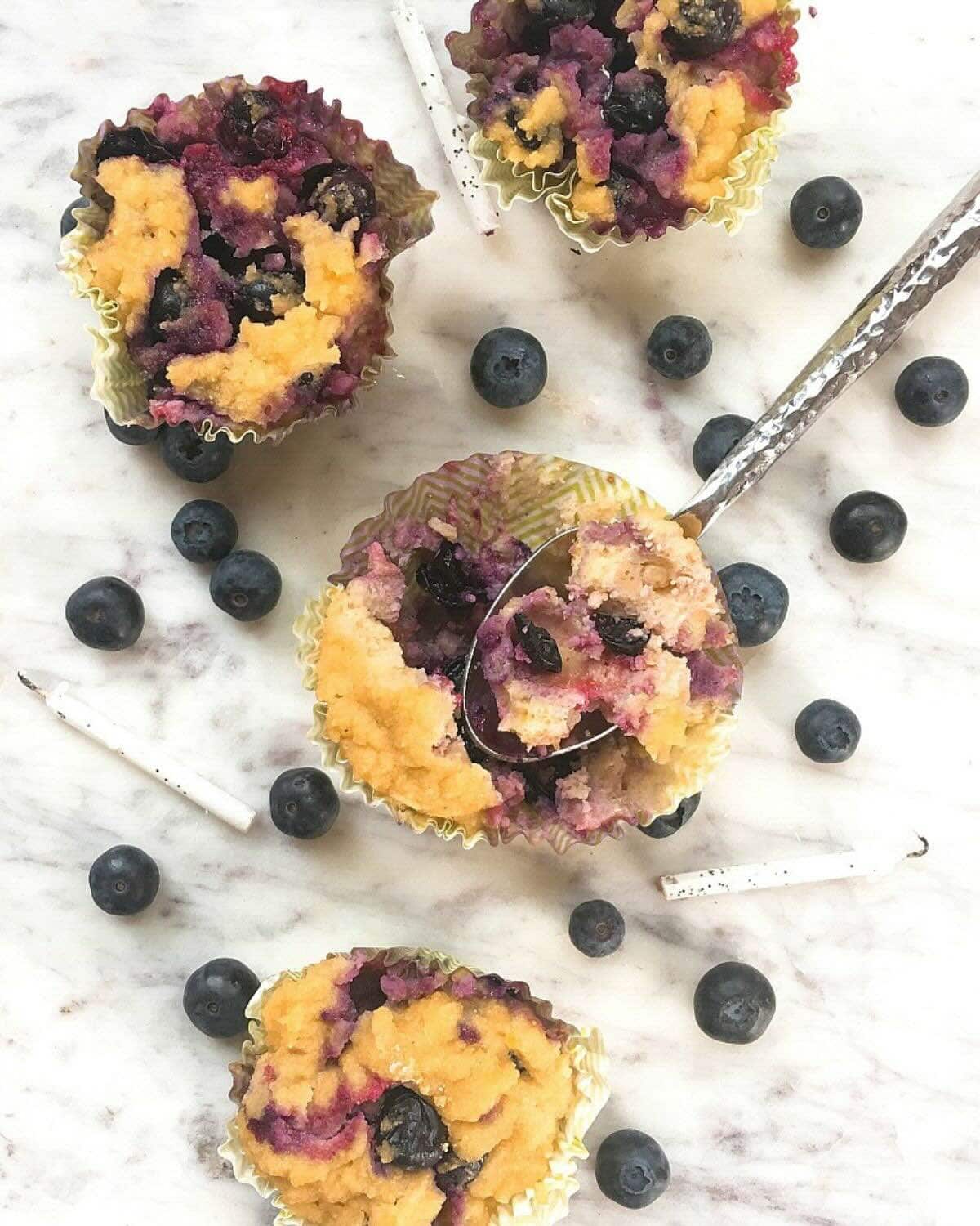 Gluten free blueberry muffins on a white marble tray with fresh blueberries in the background.