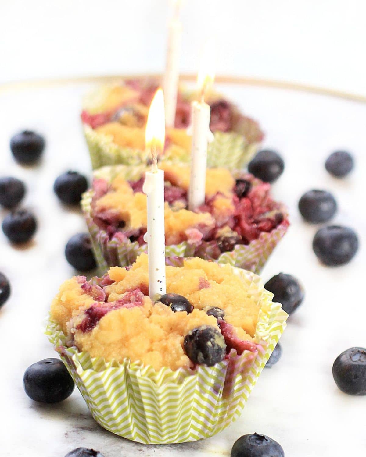 Blueberry muffins in green paper cupcake liners and topped with birthday candles.