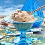Oatmeal Cookie Dough Ice Cream in a blue glass dish with a spoon sticking out.