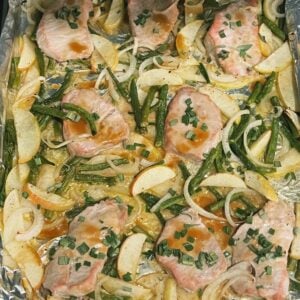 Sheet pan topped with pork chops, apples, green beans, onions, and fresh sage.