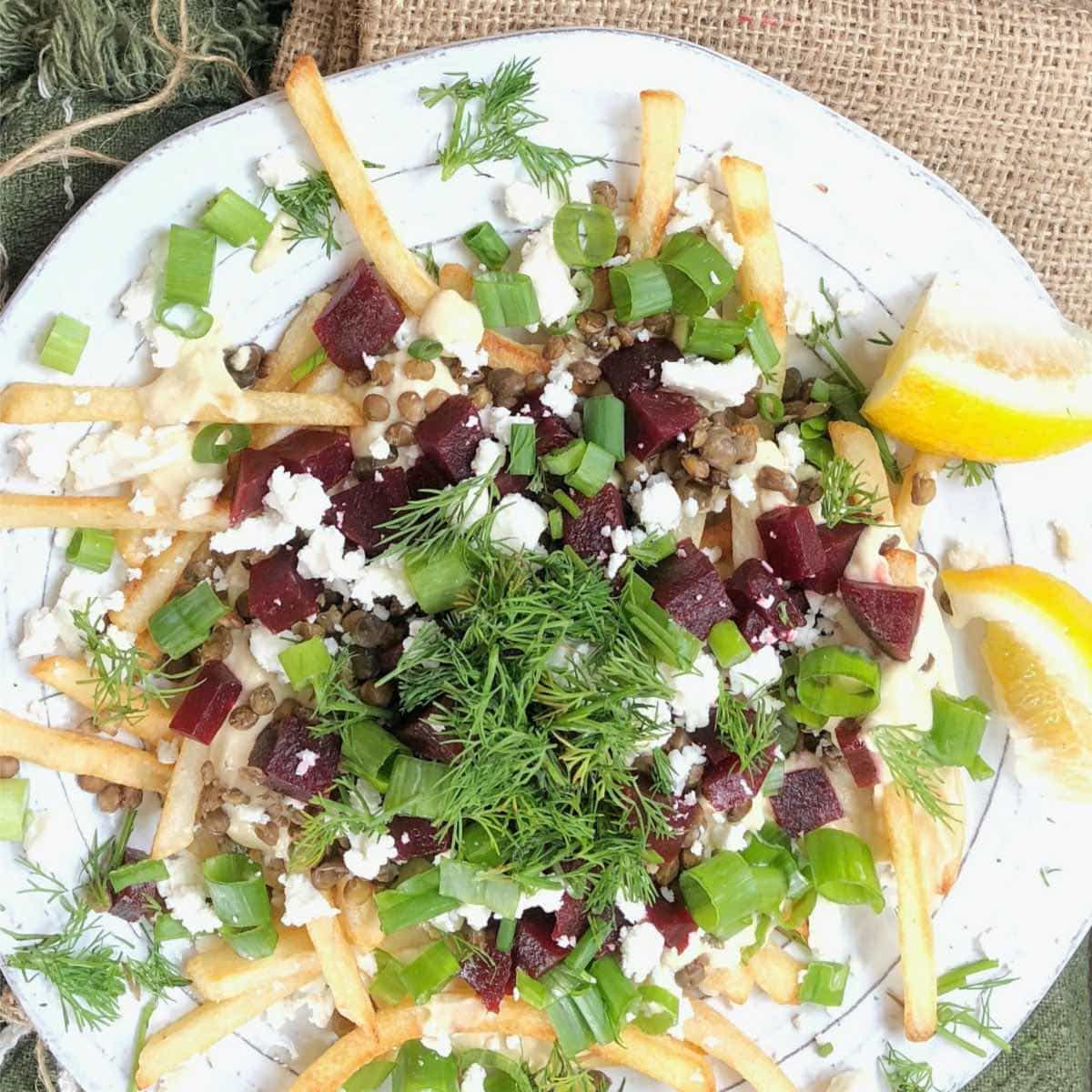 healthy loaded fries on a white plate topped with beets, feta cheese, and fresh dill