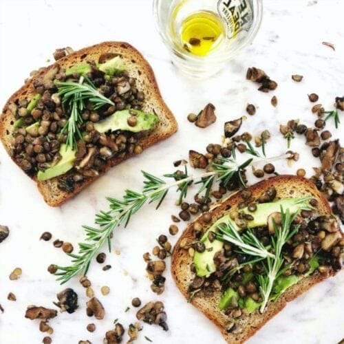 Two slices of gluten-free toast topped with lentils, mushrooms, avocado, and rosemary.