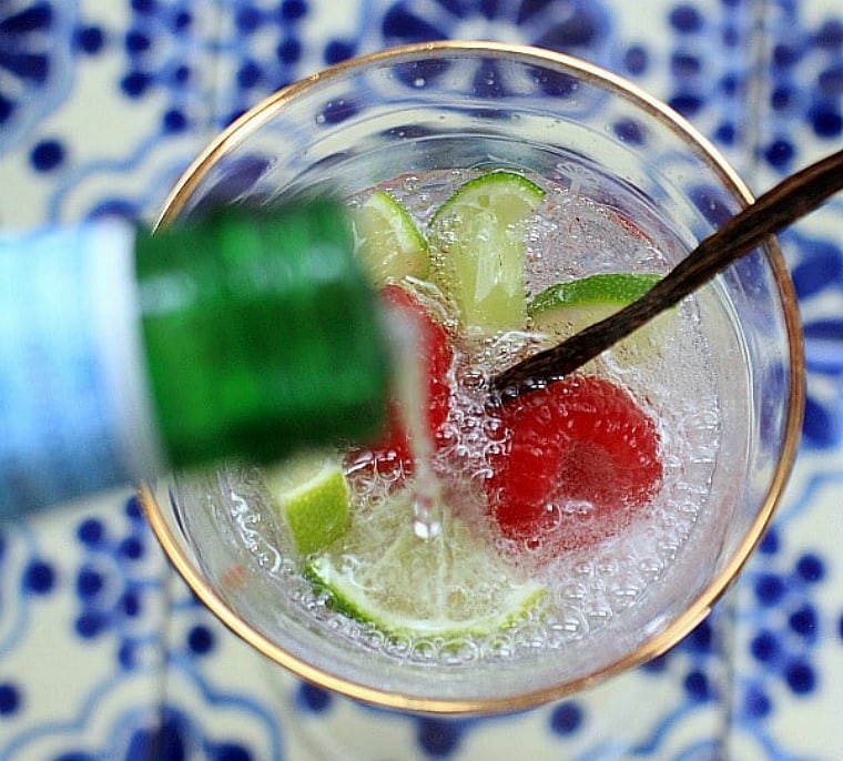 sparkling water being poured into a glass with lime and raspberries