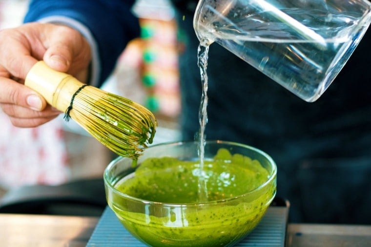 water pouring into a bowl of matcha tea and a hand holding a whisk