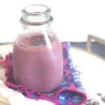 Glass jar filled with a high-protein chocolate cheesecake cherry smoothie on a pink and blue napkin.
