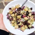Trader Joe's Cauliflower Gnocchi in a white bowl with onions, kales, pine nuts, and olive oil.