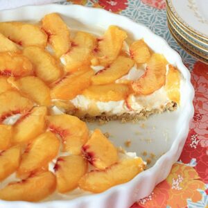 almond flour crust peach tart in a white tart pan. One slice taken out of tart.