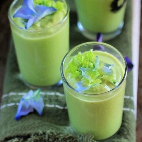 cucumber avocado soup in shot glasses with purple flowers on top.