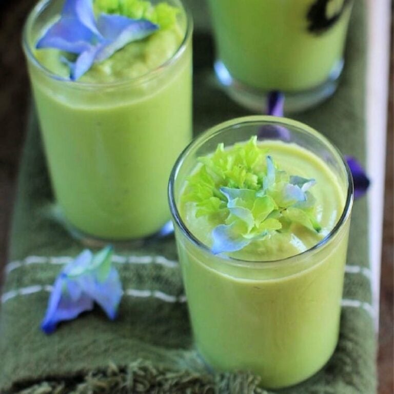 cucumber avocado soup in shot glasses with purple flowers on top.
