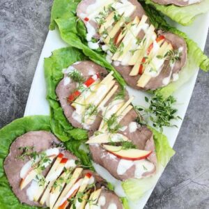 Overhead photo of 3 roast beef lettuce wraps on a white dish.