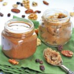 Two glass mason jars with homemade pecan butter on a green napkin and a spoon in the foreground.