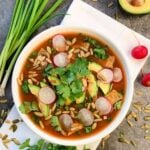 Overhead shot of a bowl of vegan tortilla soup topped with cilantro, avocado, radishes, and pumpkin seeds.