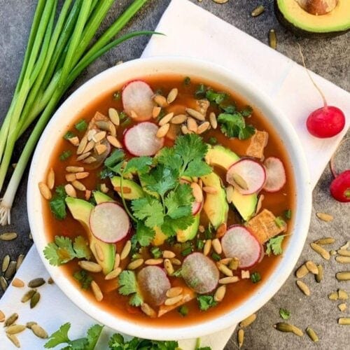 Overhead shot of a bowl of vegan tortilla soup topped with cilantro, avocado, radishes, and pumpkin seeds.