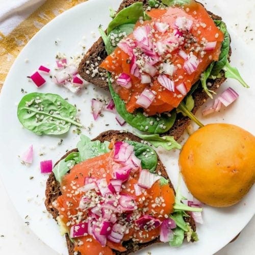 smoked salmon sandwich with greens, red onion, and hemp seeds on gluten free bread, and served on a white plate.