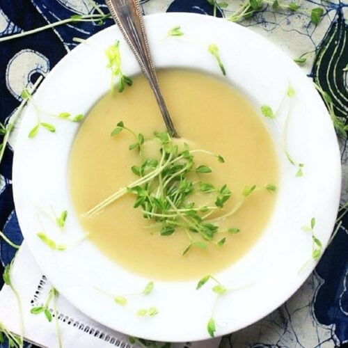 White bowl of potato leek soup on a blue background.
