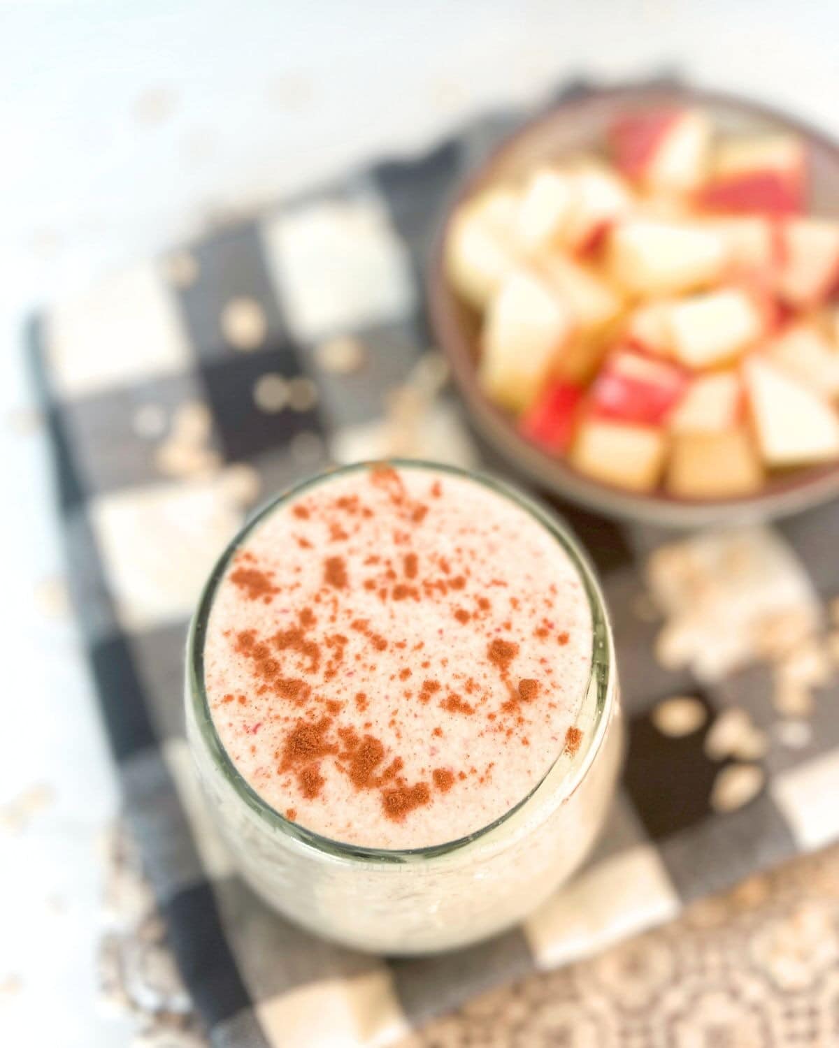 Apple smoothie topped with cinnamon on a black and white checkered napkin.