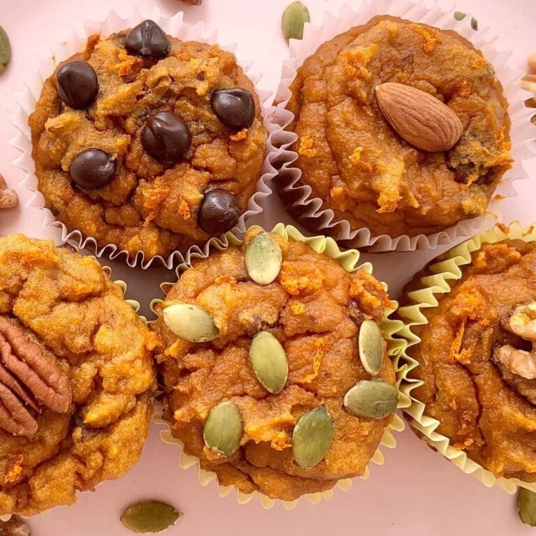 5 paleo pumpkin muffins with varios toppings including pumpkin seeds, pecans, almonds, and chocolate chips