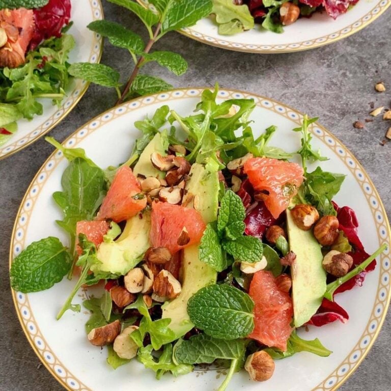 Grapefruit salad on a white plate topped with avocado and hazelnuts.