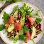 Single white plate with grapefruit salad topped with avocado and hazelnuts.