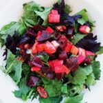 Beet apple walnut salad on top of greens in a white bowl.