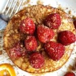 Stack of gluten free protein pancakes topped with fresh raspberries and orange zest.