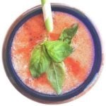 Strawberry basil lemonade topped with basil in a blue-rimmed glass with a green and white straw sticking out of the glass.